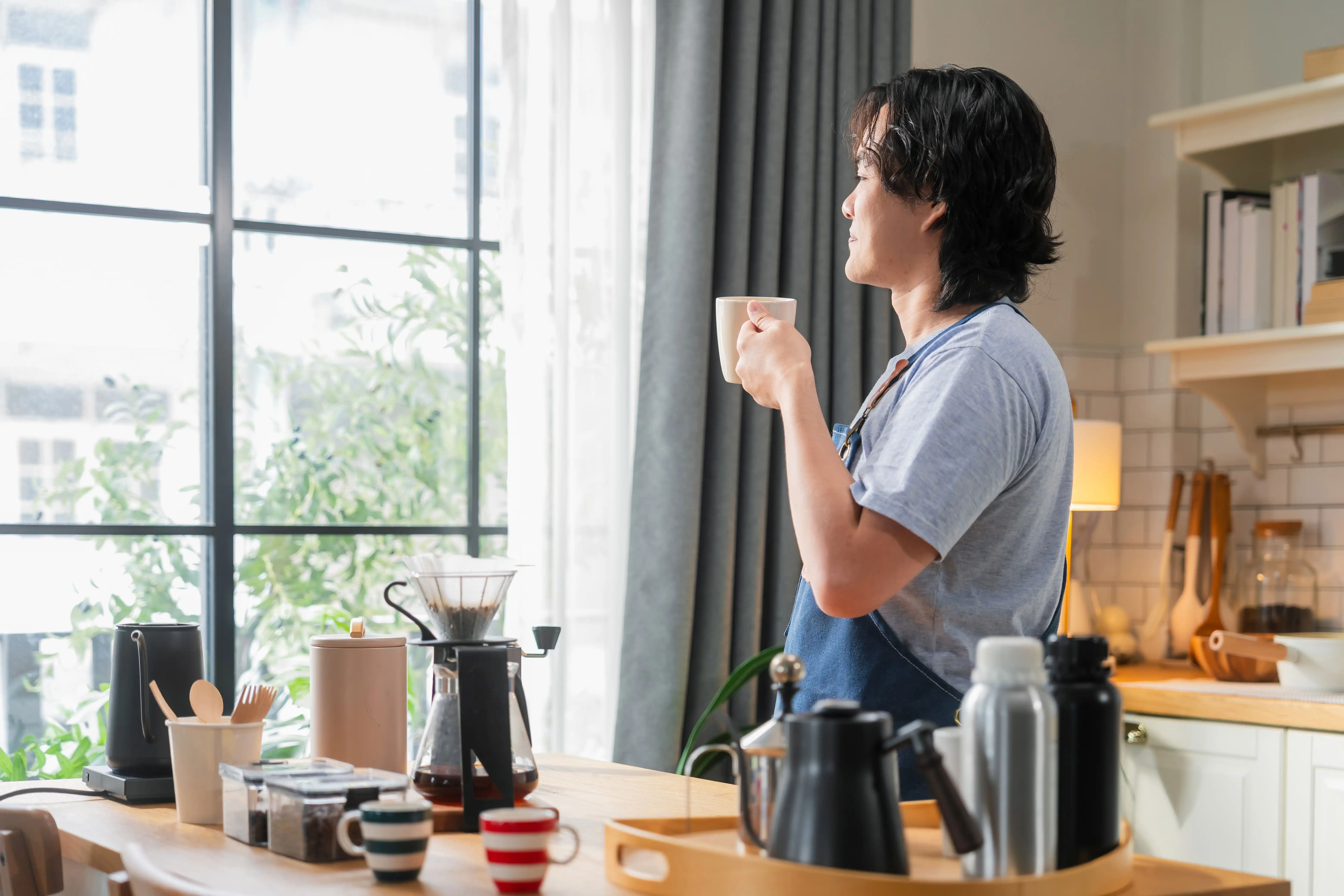 man drinking coffee looking out of kitchen window onto a city street