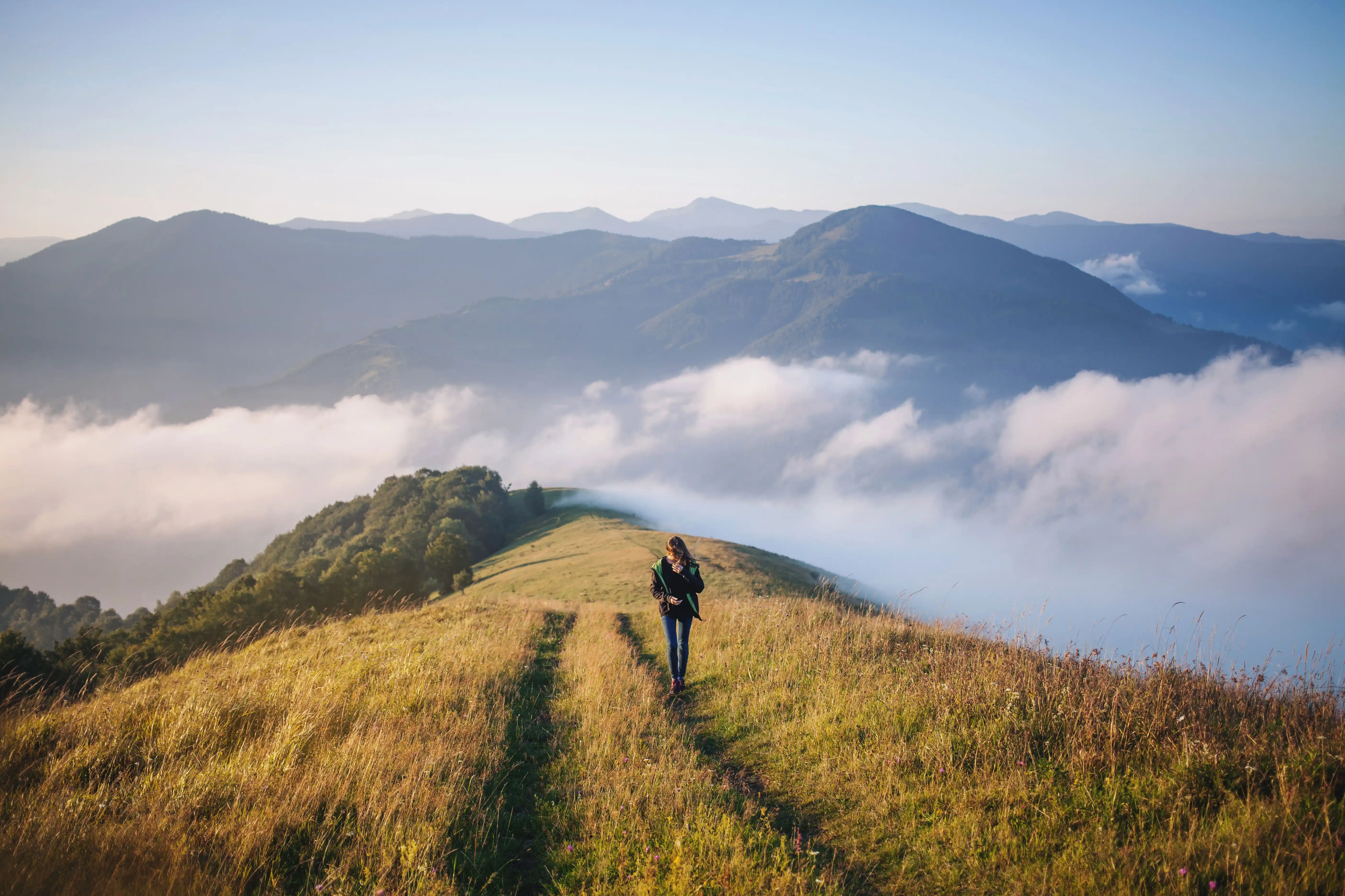 a young woman walking along the centre of a hiking trail on the top of a peak in the UK