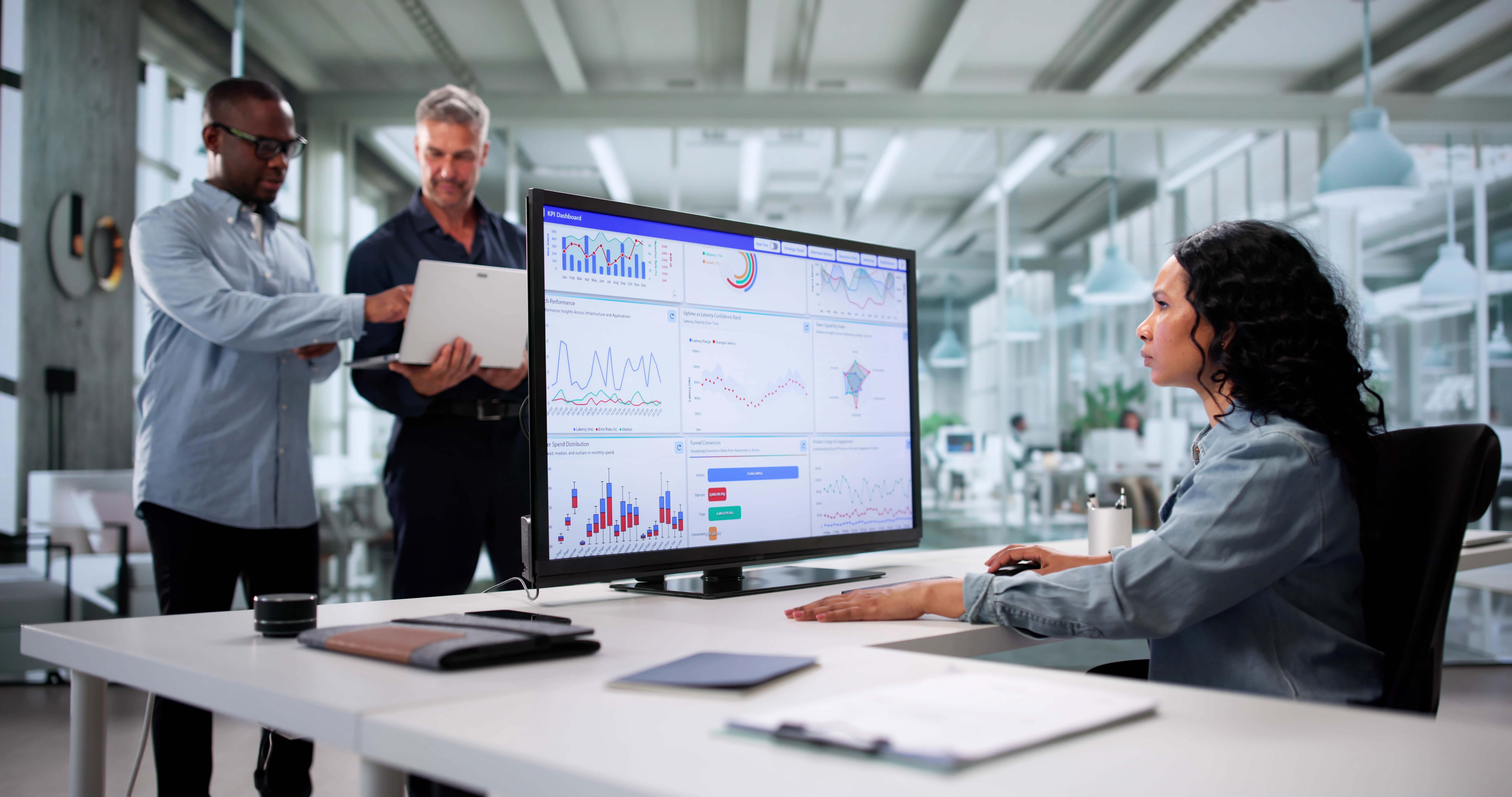 a female credit risk analyst reviewing financial data for a loan application on a computer screen while two male colleagues review data on a laptop in the background